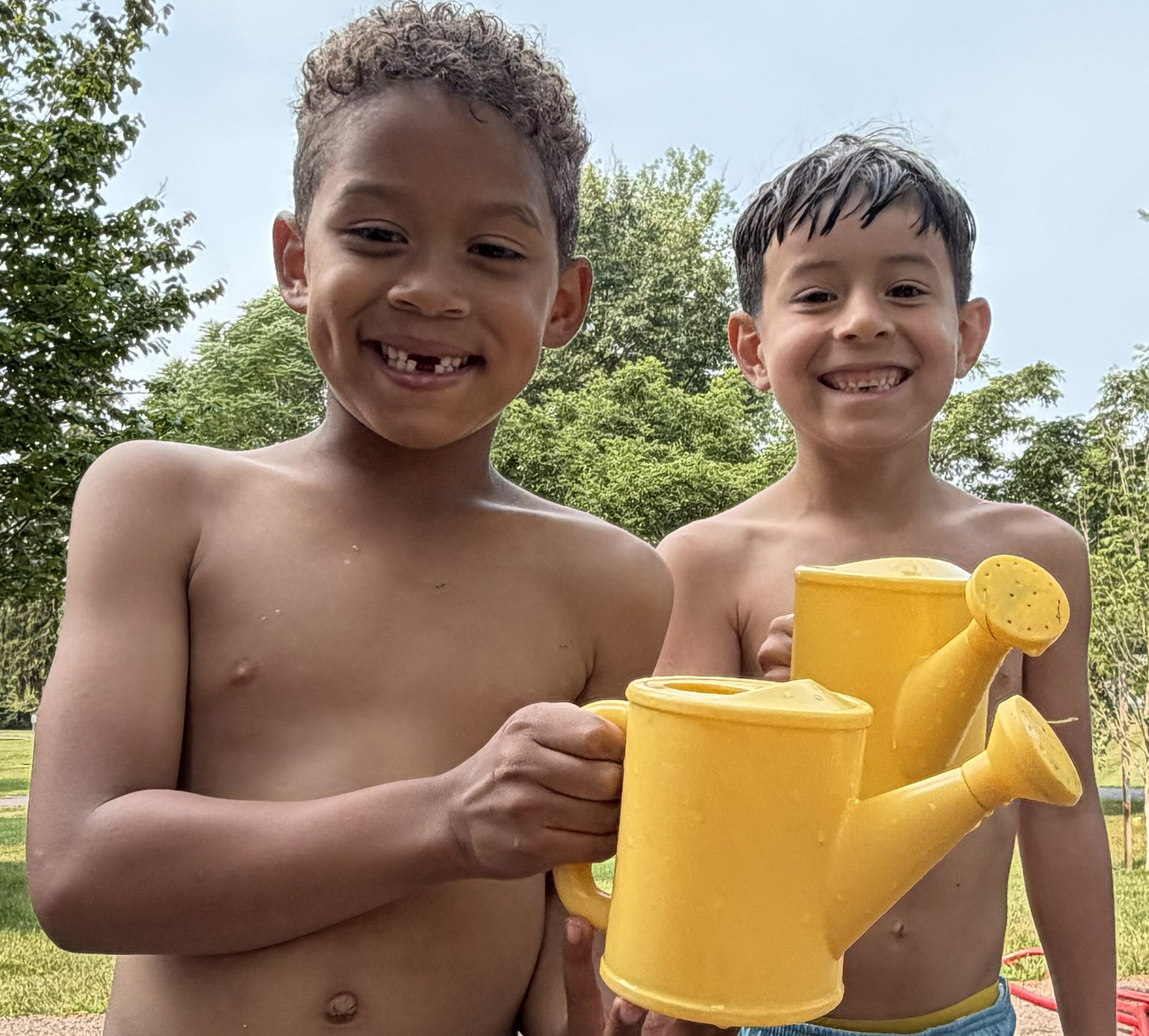 Two boys grinning and holding yellow watering cans